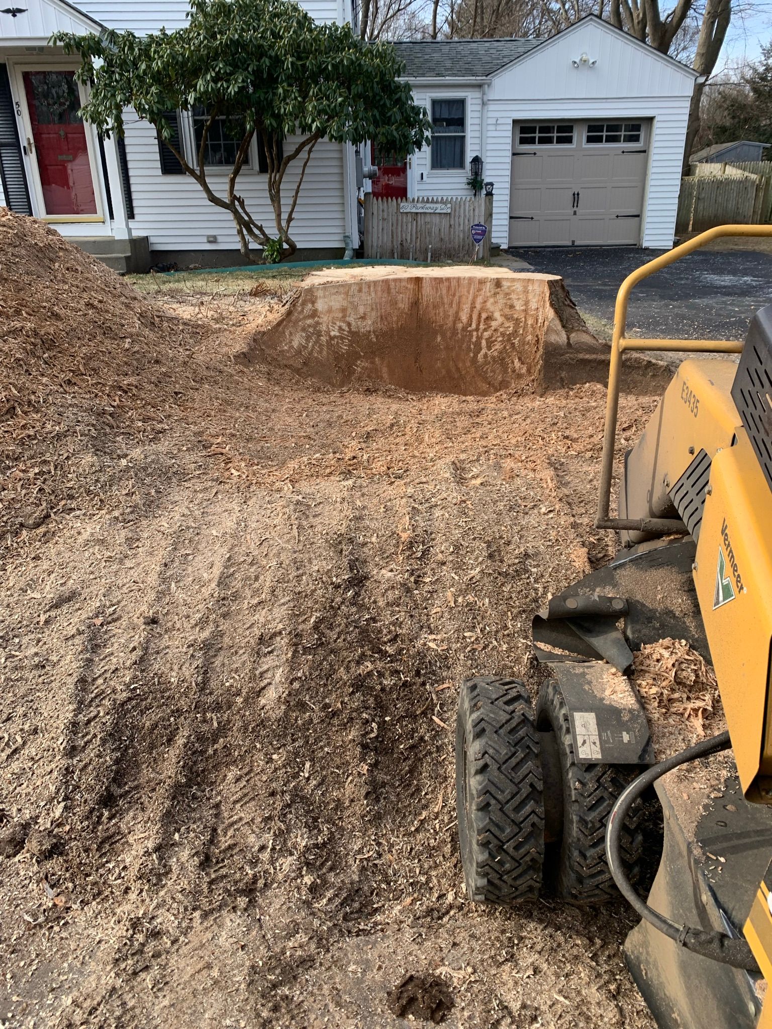 A stump grinder is working on a tree stump in front of a house.