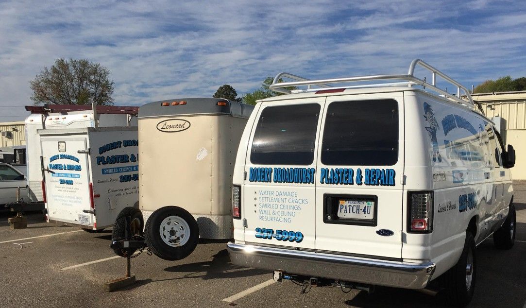 White work vans and a trailer with business logos parked in a lot under a cloudy sky.