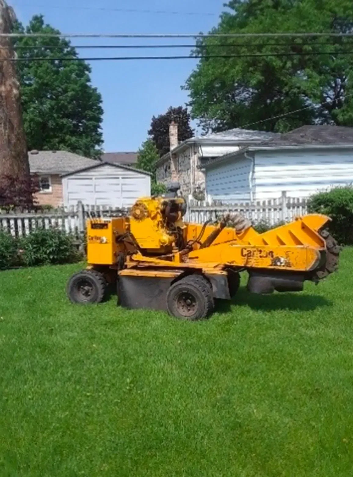 Yellow stump grinder on grassy lawn, ready for use near a residential area.