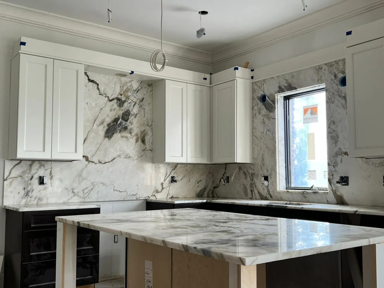a kitchen with white cabinets , marble counter tops, and a large island