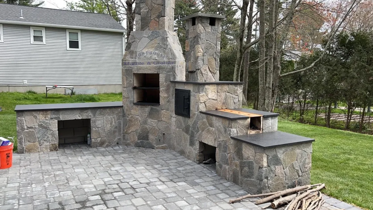 a stone fireplace is sitting on a patio next to a house