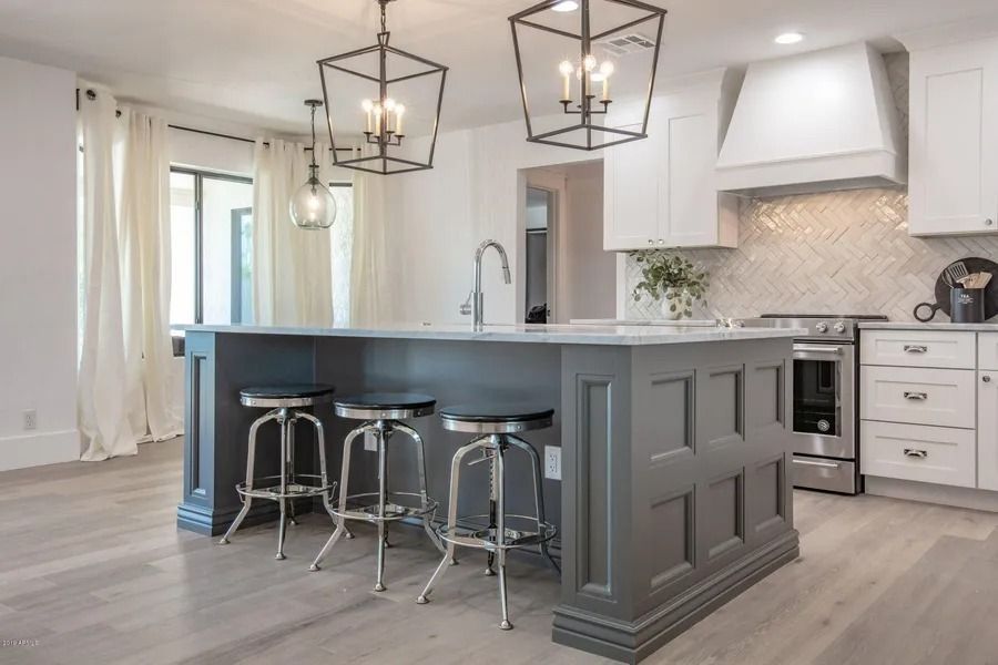 Gray kitchen island with three stools, white cabinets, and lantern pendant lights.