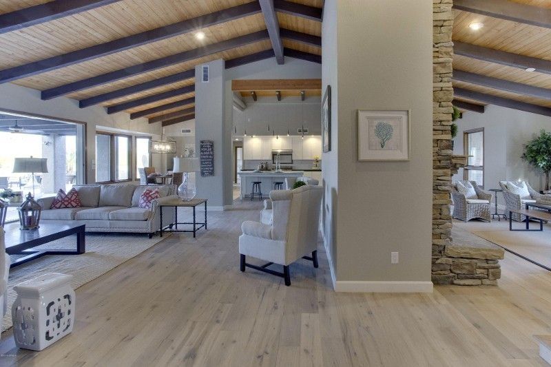 Spacious living room with wood beams, light wood floors, and stone fireplace, leading to dining and kitchen areas.