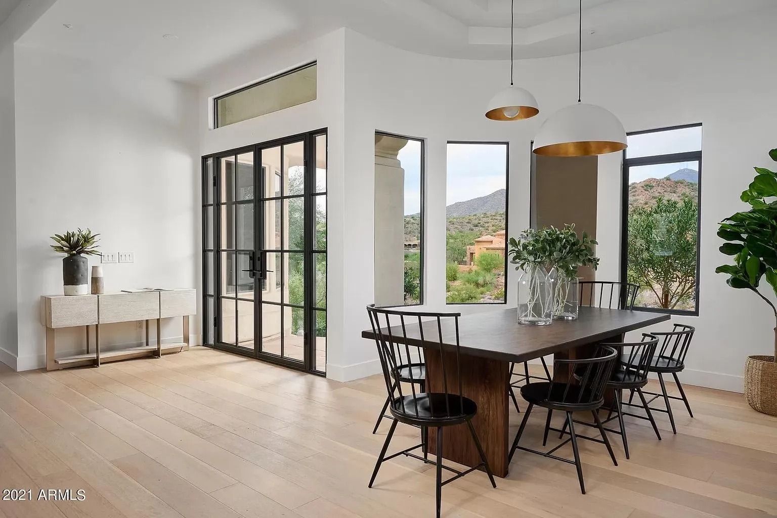 Dining room with a wooden table, black chairs, and large windows overlooking a scenic view.