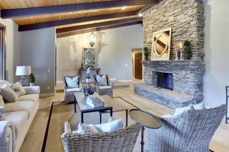 Living room with stone fireplace, wood beams, light wood floors, and neutral-colored furniture.