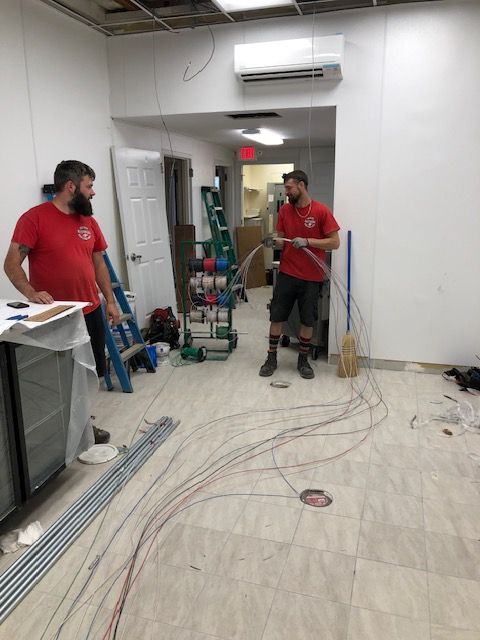 Two men are standing in a room with a lot of wires on the floor.