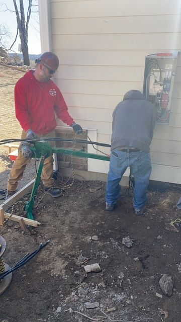 Two men are working on a electrical box on the side of a house.