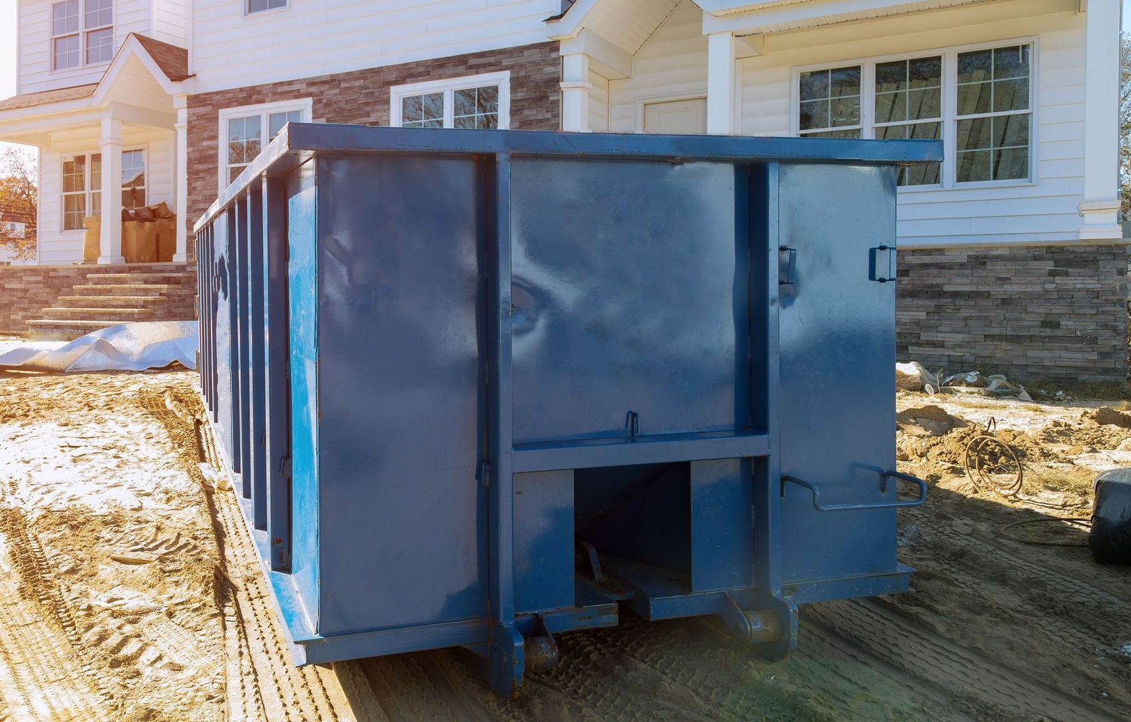 A blue dumpster is parked in front of a house under construction.