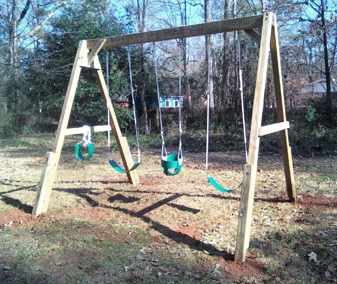 A wooden swing set with green swings in a yard