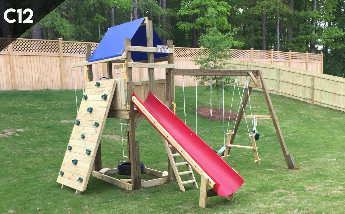 A wooden playground with a red slide , swings , and a climbing wall.