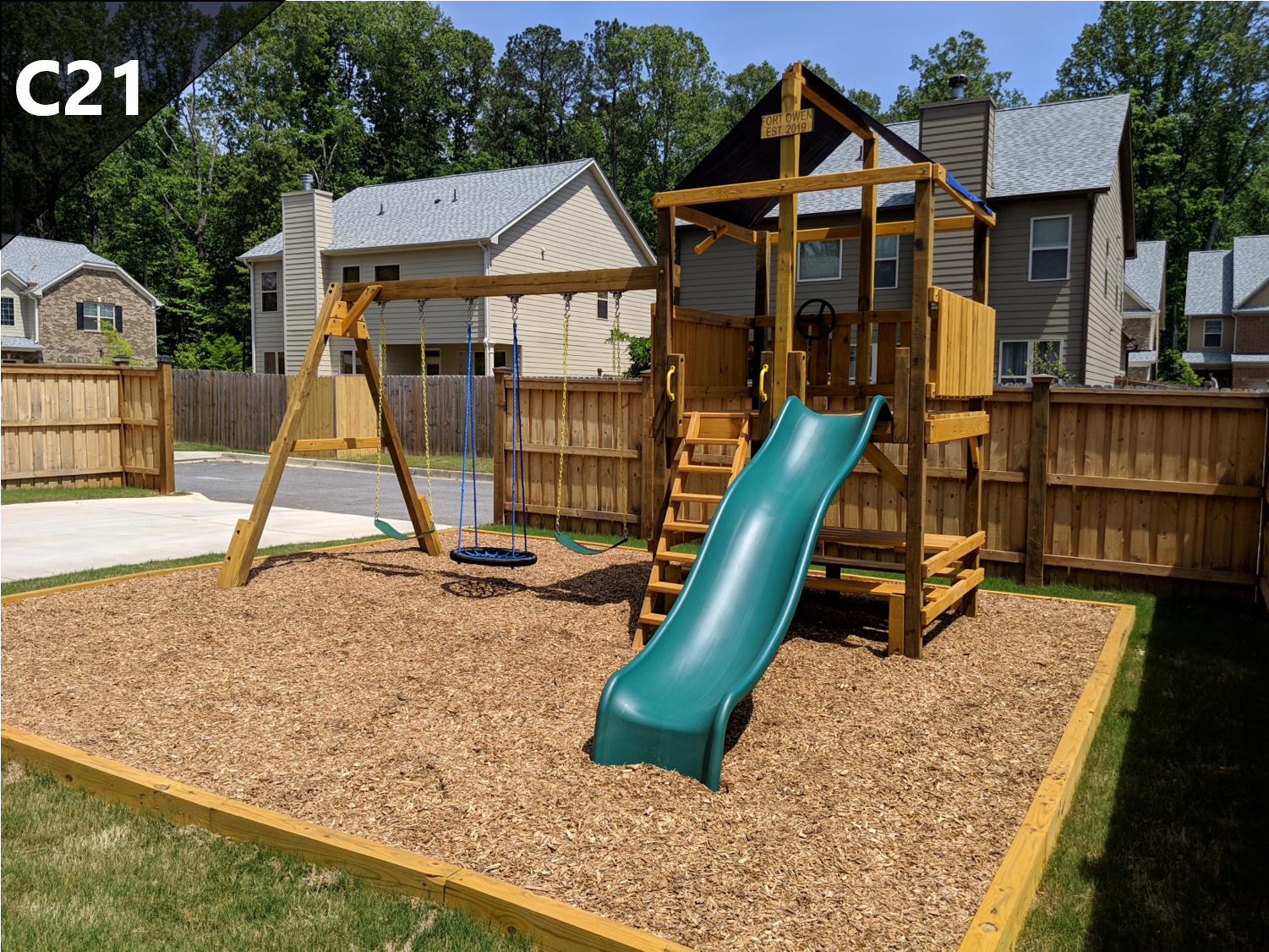 A wooden playground with a green slide and swings in a backyard.