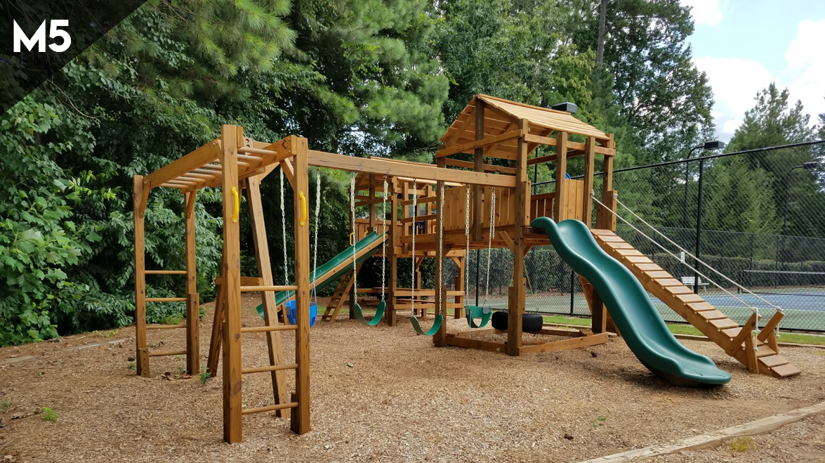 A wooden playground with a slide and swings in a park.