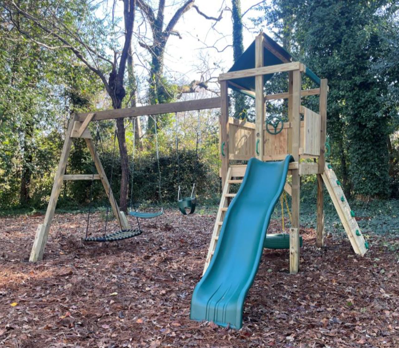 A wooden playground with a blue slide and swings