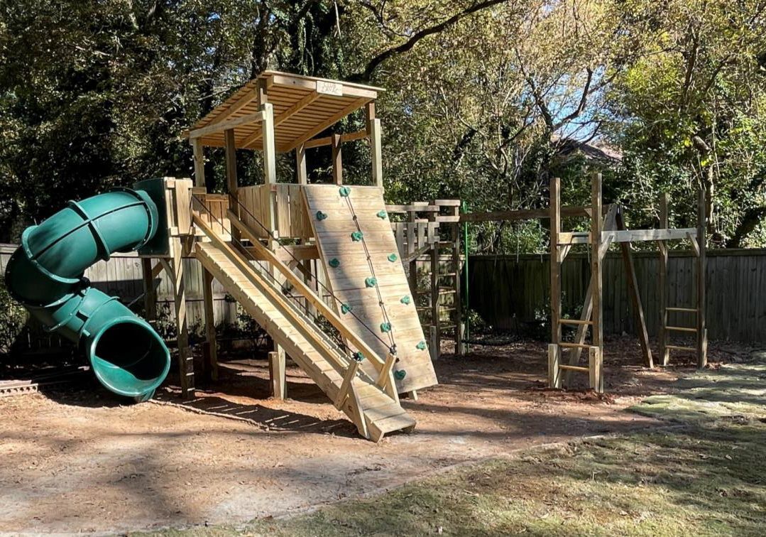 A wooden playground with a green slide and a climbing wall.