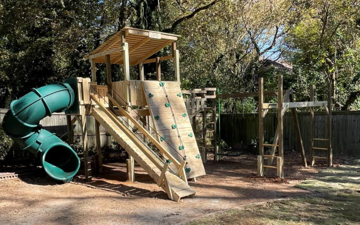 A wooden playground with a green slide and a climbing wall.