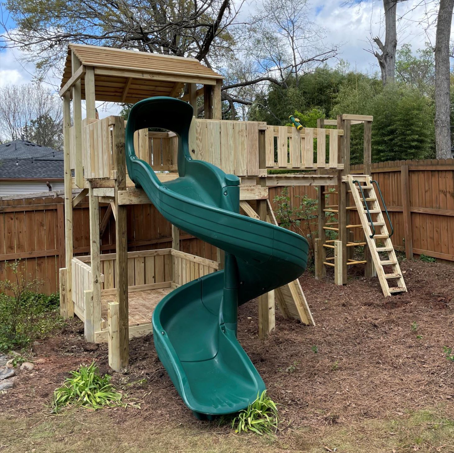 A wooden playground with a green slide and stairs