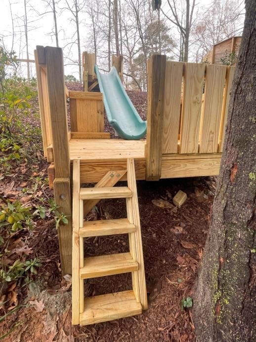 A wooden playground with a slide and stairs attached to a tree.