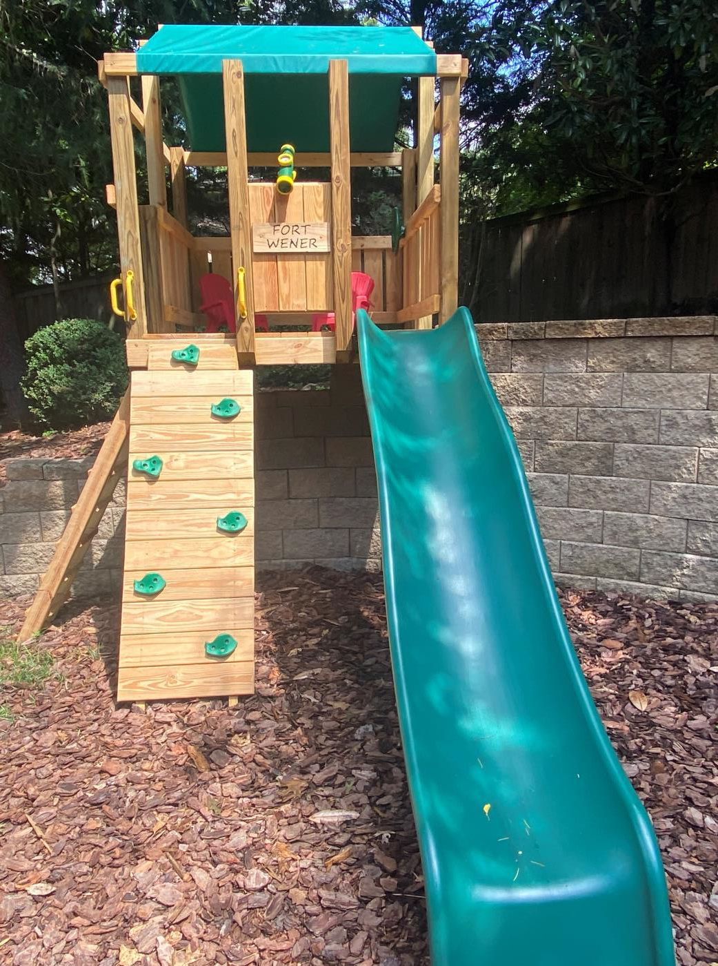 A wooden playground with a slide and climbing wall.