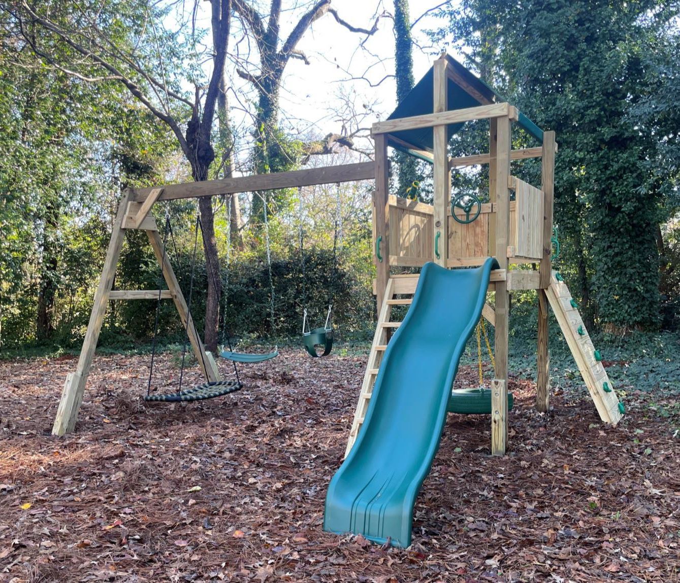 A wooden playground with a blue slide and swings