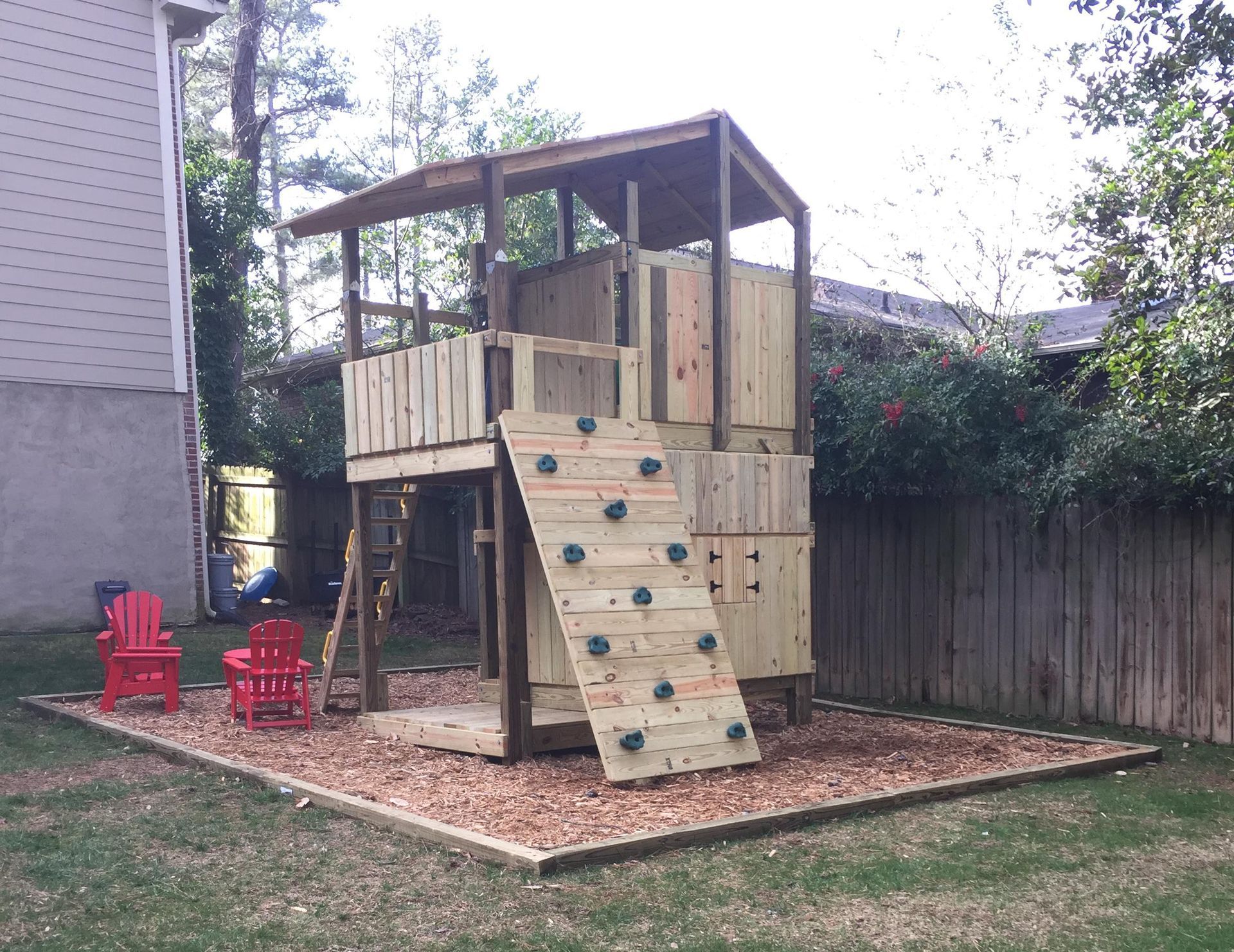 A wooden playground with red chairs in front of a house