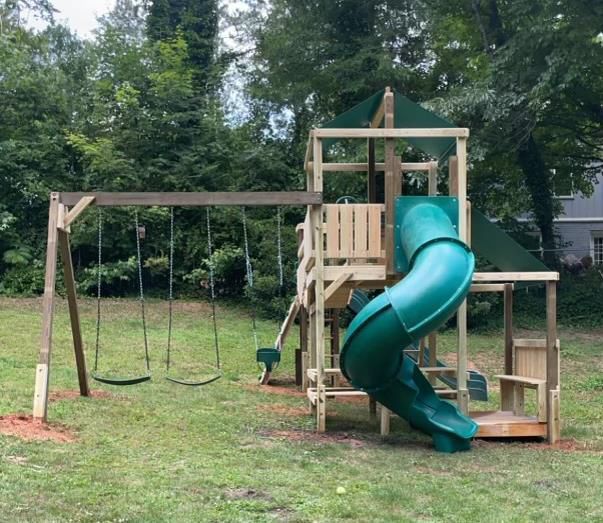 A wooden playground set with a green slide and swings.