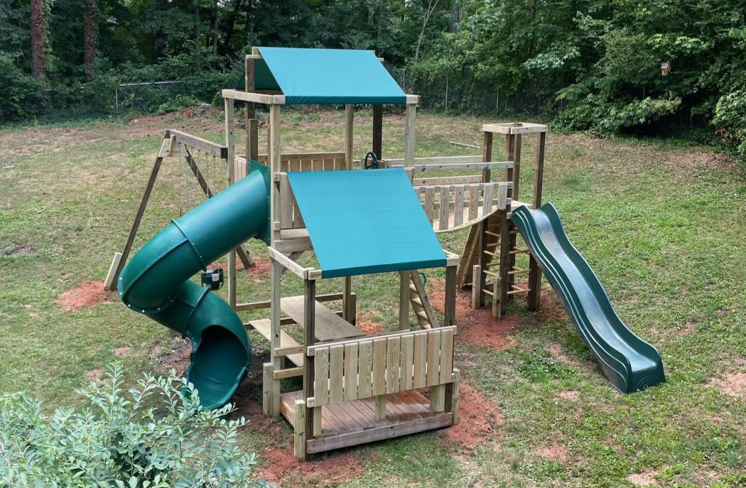 A wooden playground with a green slide and swings in a backyard.