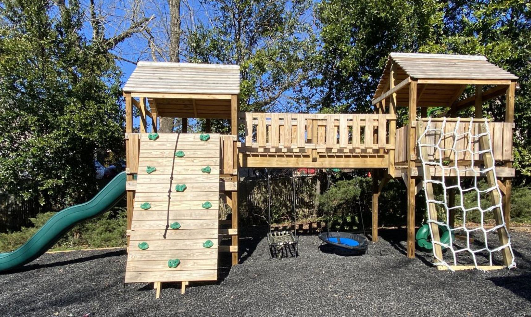 A wooden playground with a slide and a climbing wall.