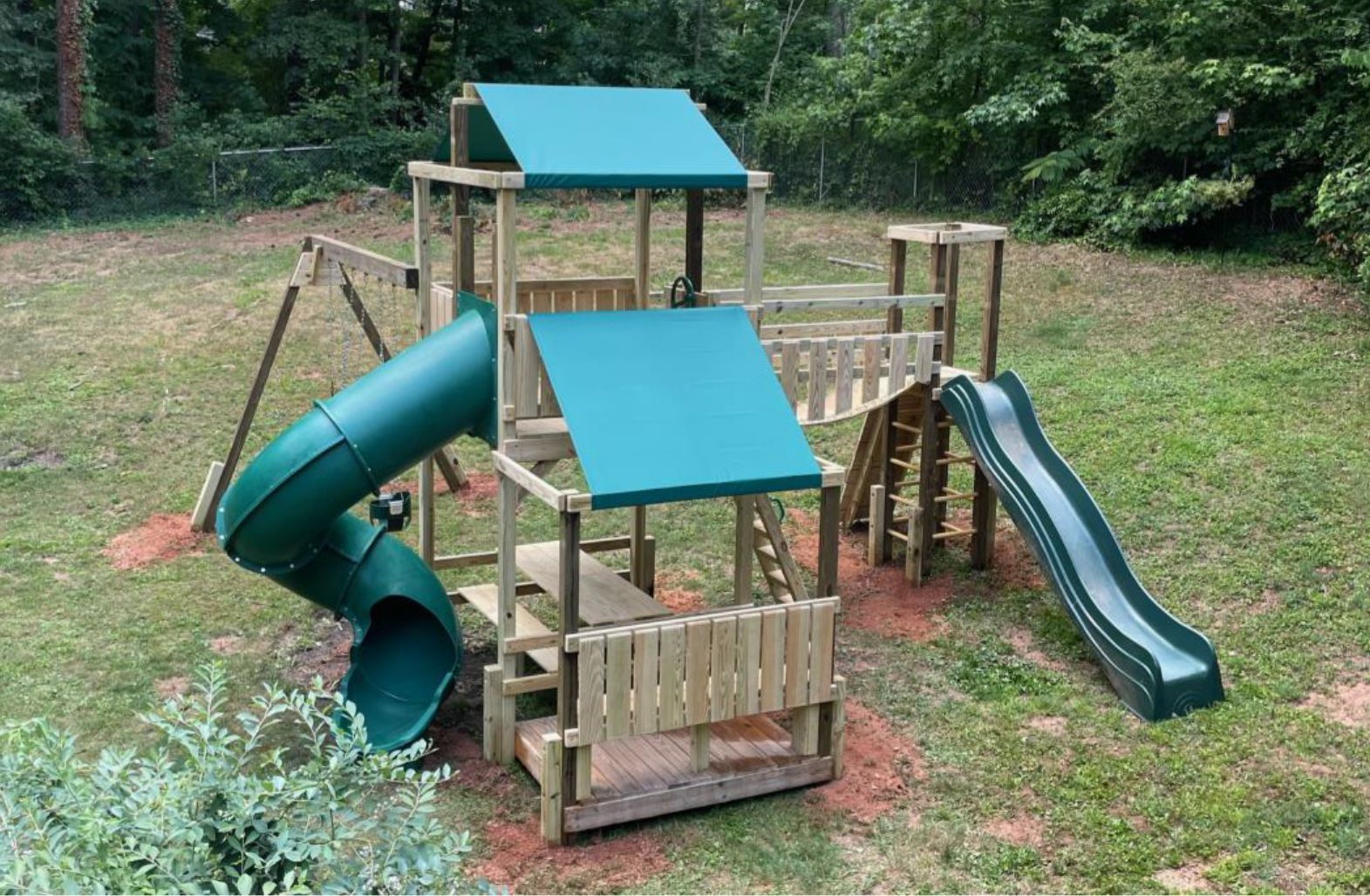 A wooden playground with a green slide and a green canopy