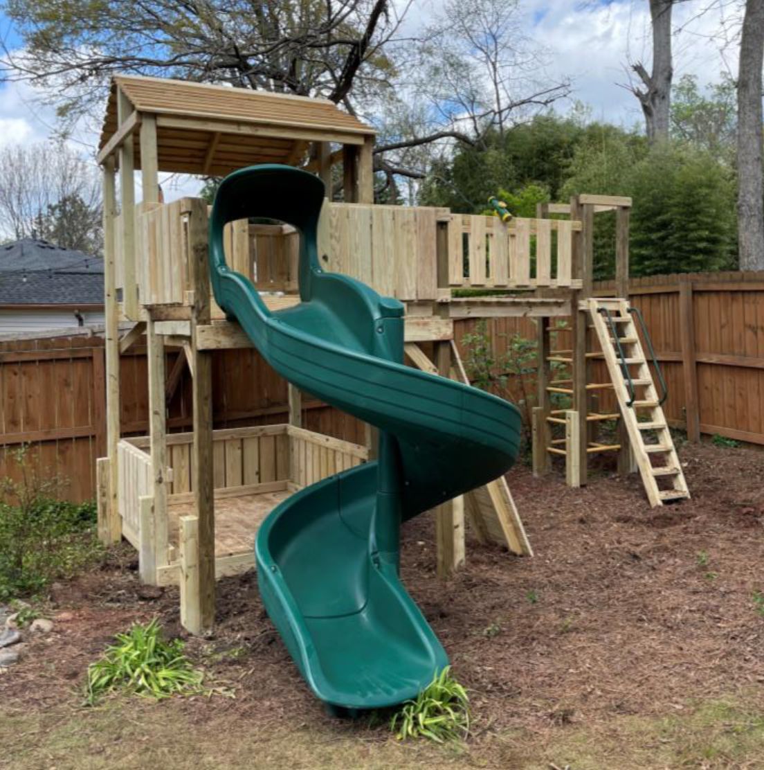 A wooden playground with a green slide and stairs