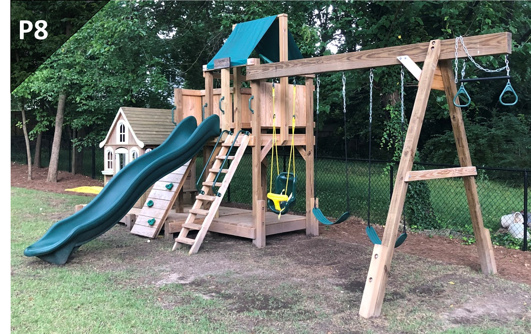 A wooden playground with a slide , swings , and a climbing wall.