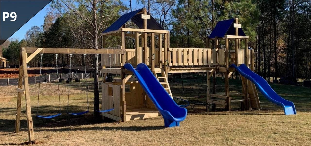 A wooden playground with blue slides and swings in a park.