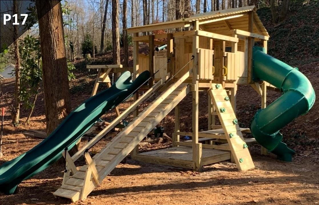 A wooden playground with a green slide and stairs in the woods.