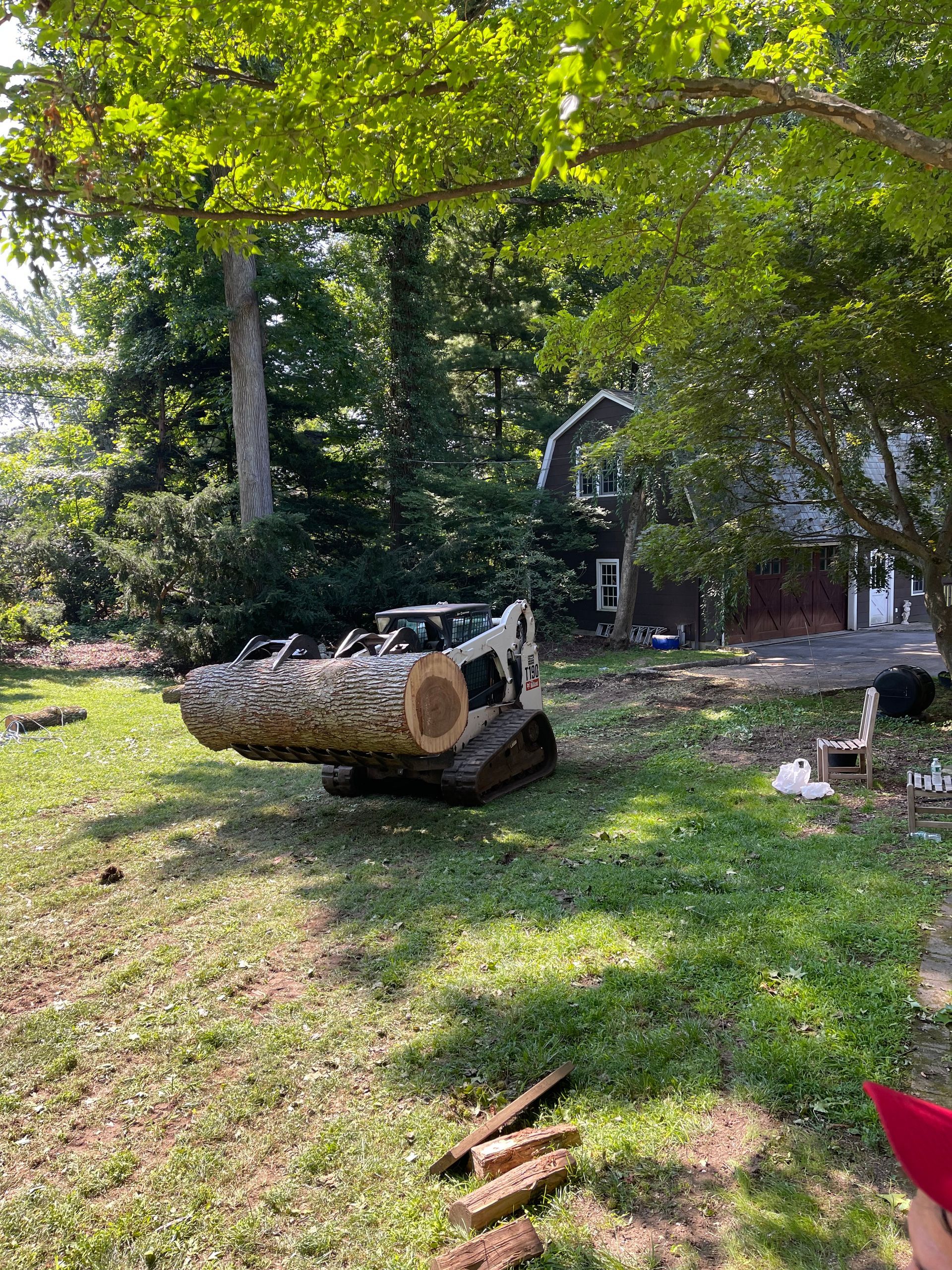 A large log is sitting on top of a tractor in a yard.