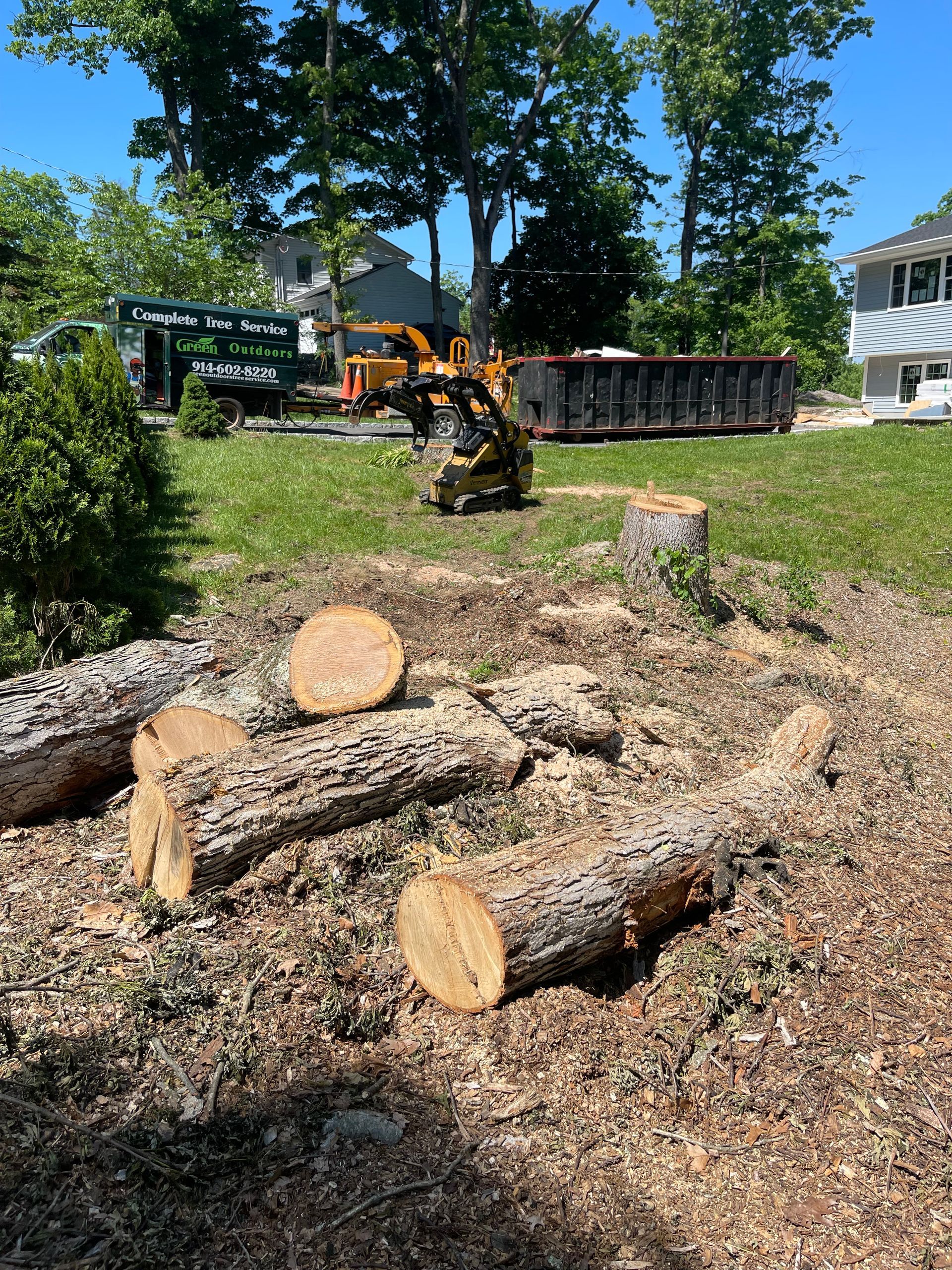 A pile of logs in a yard with a truck in the background.