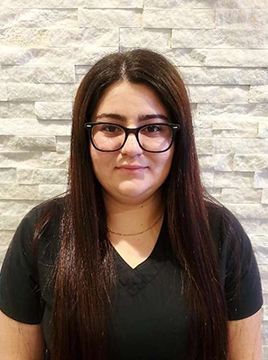 A woman wearing glasses and a black shirt is standing in front of a brick wall.