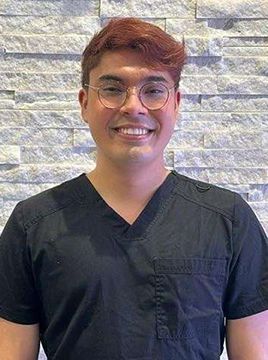 A young man wearing glasses and a black scrub top is smiling for the camera.