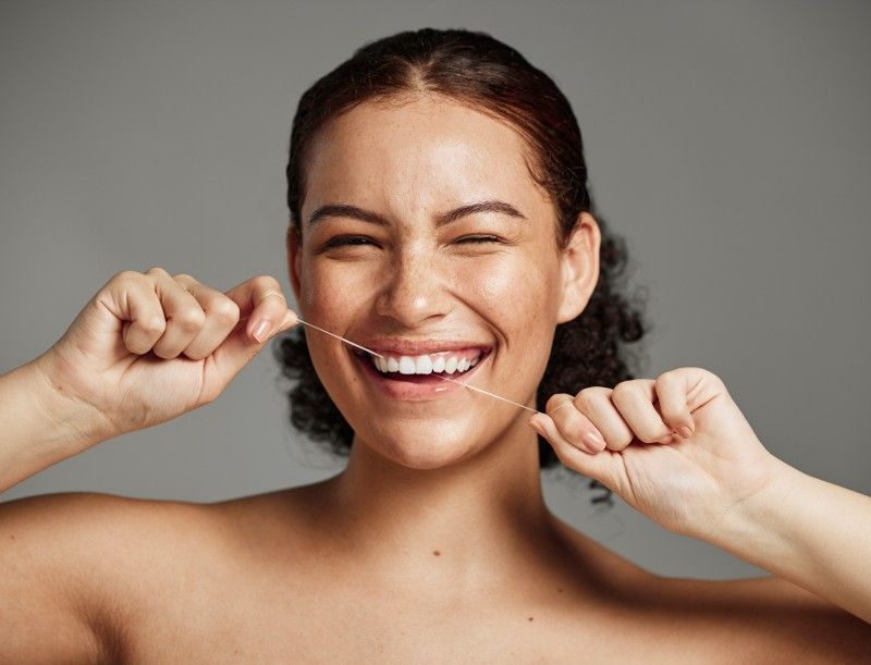 A woman is flossing her teeth and smiling.