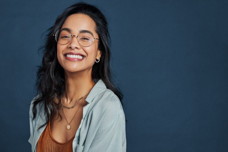 A woman wearing glasses and a necklace is smiling.