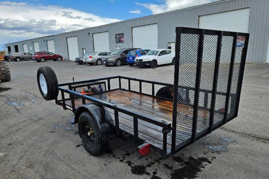 Black utility trailer with ramp gate parked outside an industrial warehouse