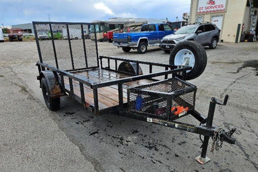 Utility trailer with mesh sides and a spare tire parked in a lot, viewed from the front-right.
