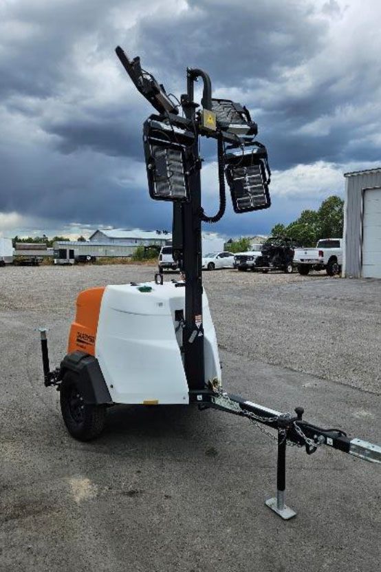 Mobile portable light tower trailer with raised lamps on a gravel lot under cloudy sky