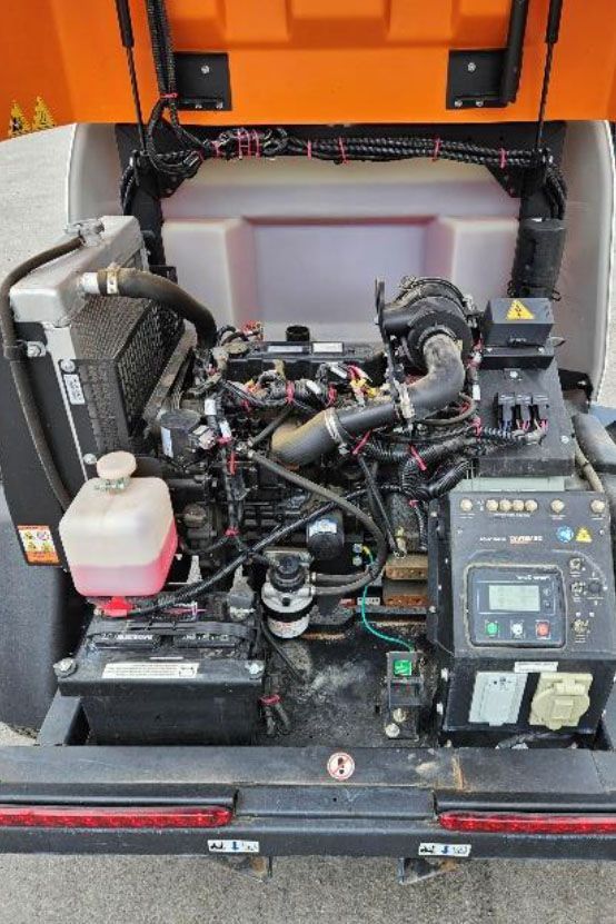 Compact engine or generator compartment with wiring, hoses, and control panel inside an orange enclosure