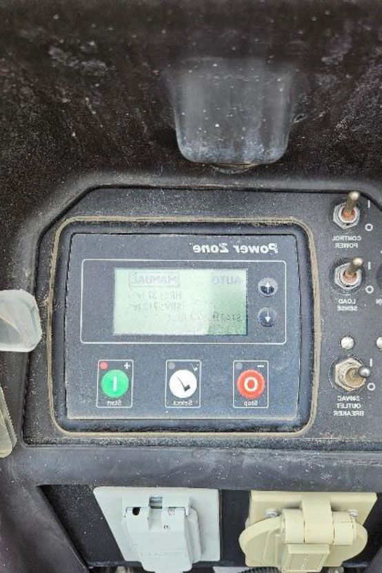 Close-up of a dusty control panel with a digital display, buttons, and switches on black equipment.