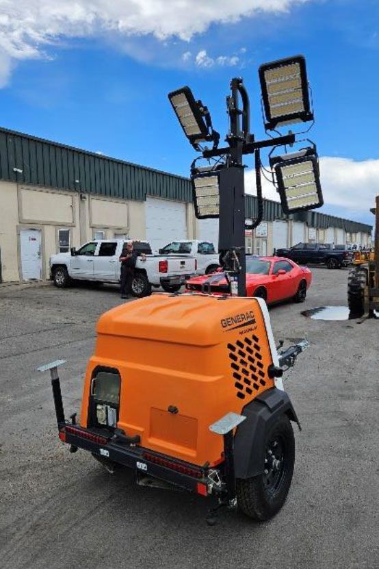 Orange portable light tower on a trailer in an industrial parking lot with raised floodlights under a blue sky