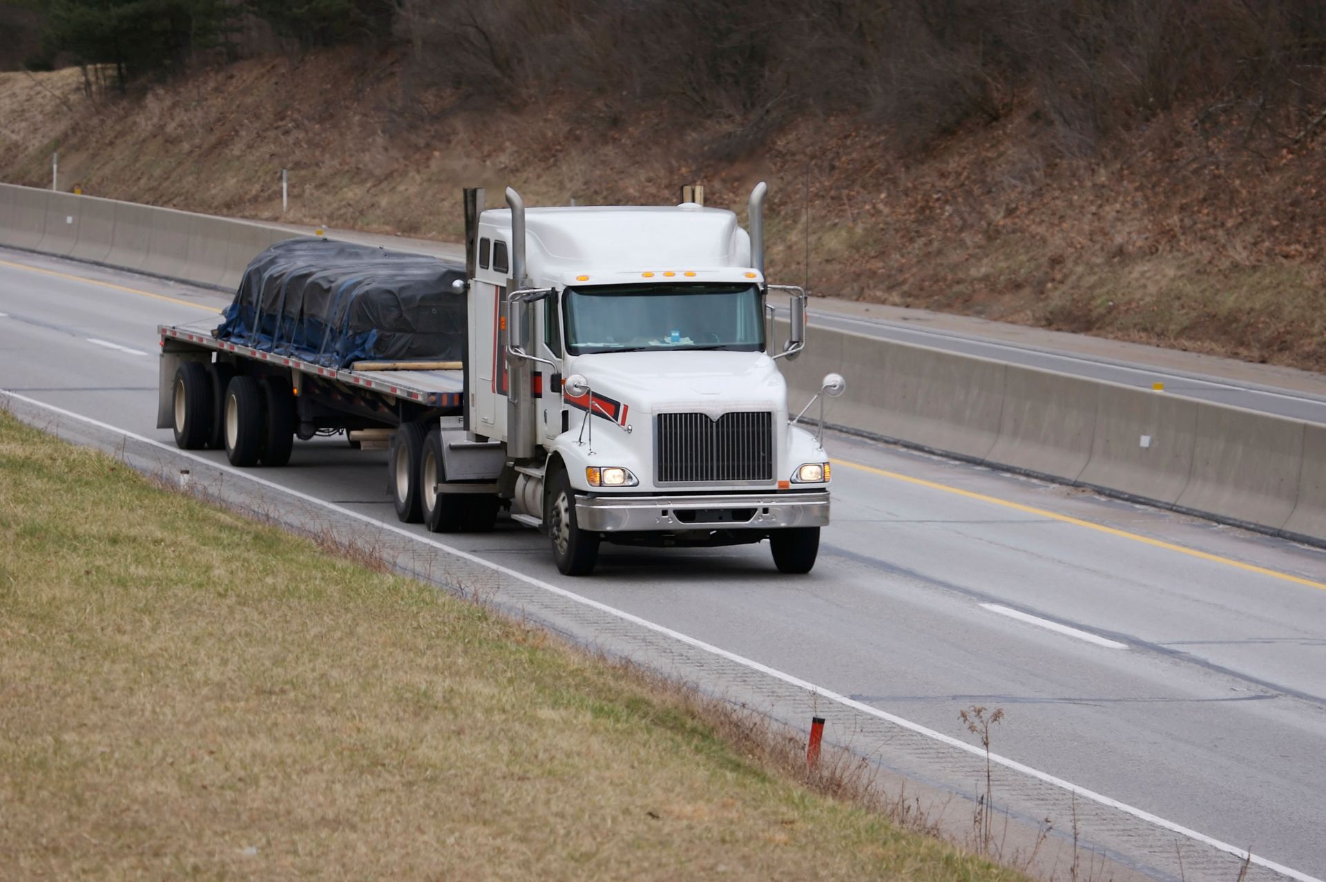 White semi-truck hauling a covered load on a wet highway lane