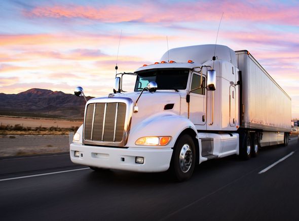 White semi-truck driving on a highway at sunset with mountains in the background