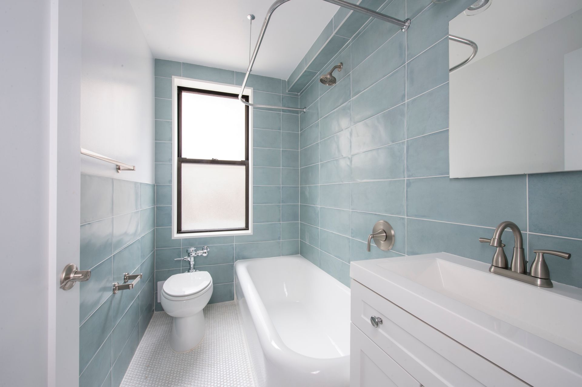 Bright blue-tiled bathroom with bathtub, toilet, sink vanity, and window