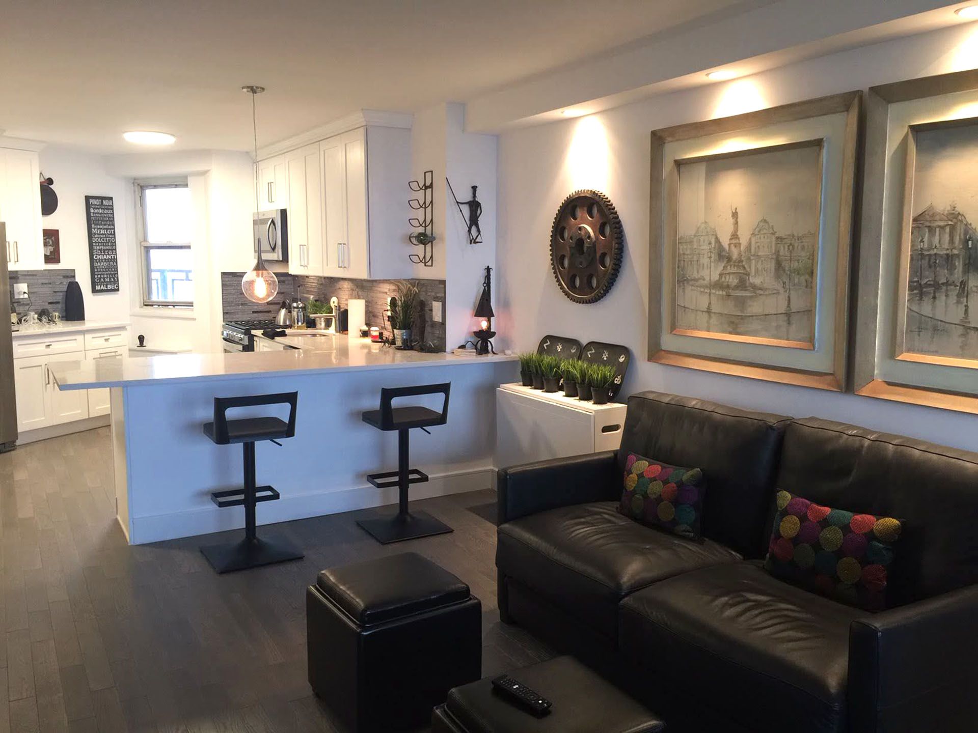 Modern living room with black leather sofa, white kitchen island, bar stools, and framed wall art