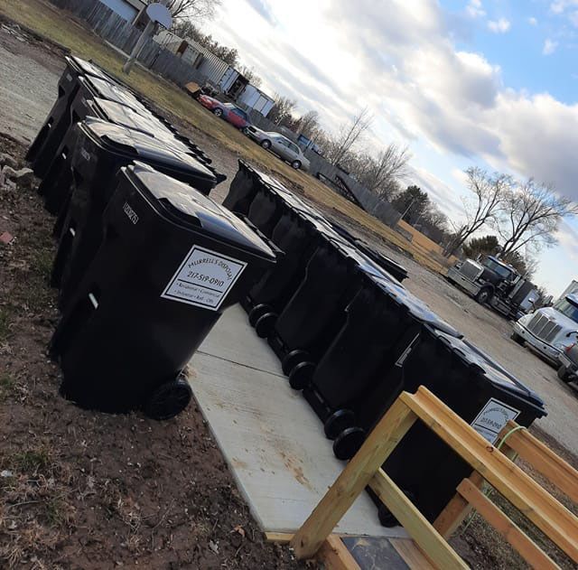 A row of black trash bins on a concrete pad.