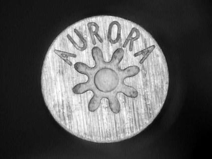 Aurora metal button with a sunburst symbol and engraved text on a dark background